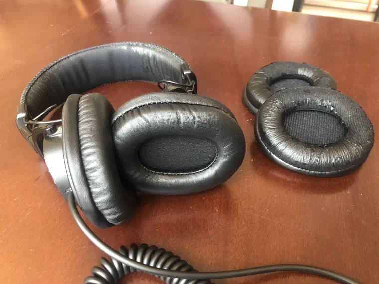 Sony MDR-V6 headphones with new black ear pads fitted, beside the two original pads, cracked and peeling.